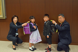 写真：教育長、市長が子どもたちにランドセルカバーを付ける様子