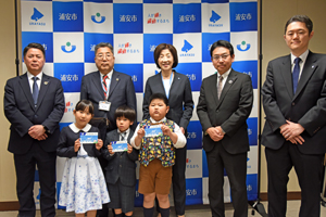 写真：読書通帳を持った新小学校1年生3人と寄贈してくださった京葉銀行の皆さん、市長、教育長