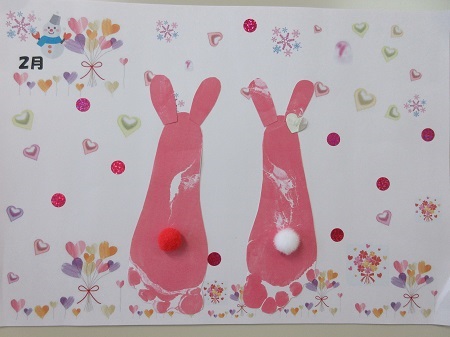 制作する足形カードのイメージ。ピンク色の足形にウサギをかたどった耳や尻尾などのかざりをつけ、隅に雪だるまのイラストと共に「2月」と記載されています。