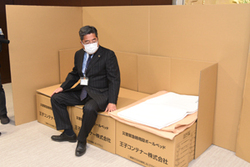 写真：段ボールベッドの座り心地を確かめる内田市長