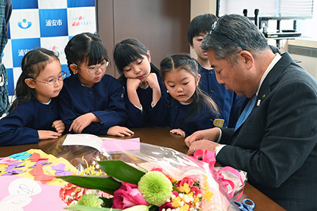 市長が折り紙を折っている様子を見る園児たち