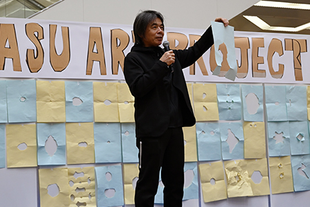 写真：穴の開いた紙を持つ日比野学長